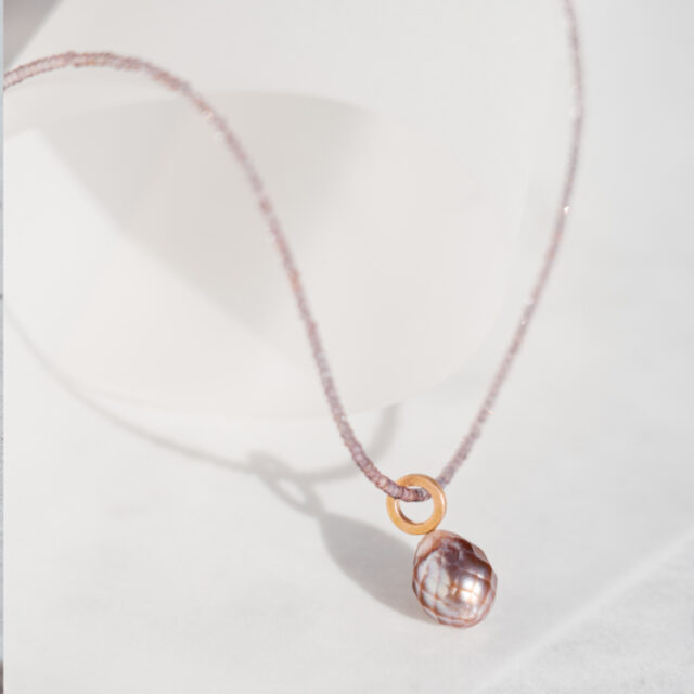 Perle mit Facetten in einem rosa Ton als Anhänger an einer Steinkette