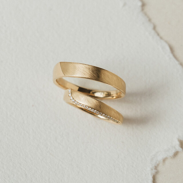 Zwei Eheringe in 585 Gelbgold, der Damenring schmaler mit langer Brillantlinie