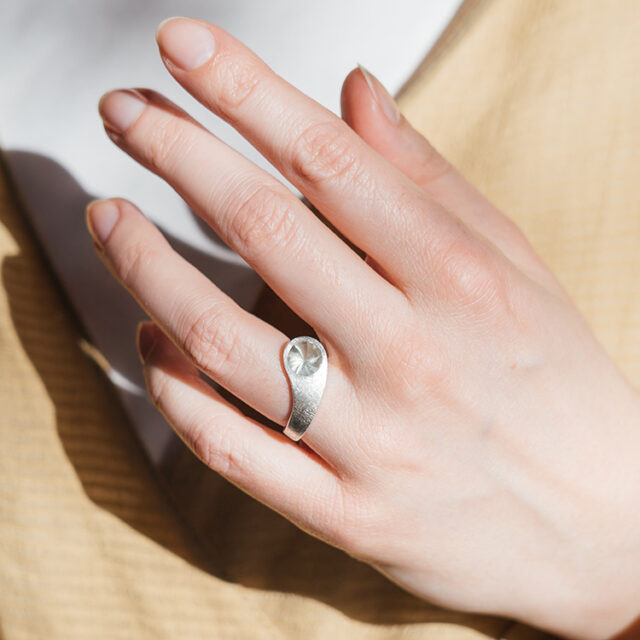 Silberner Ring mit leicht transparentem grauen Stein an einer Hand.