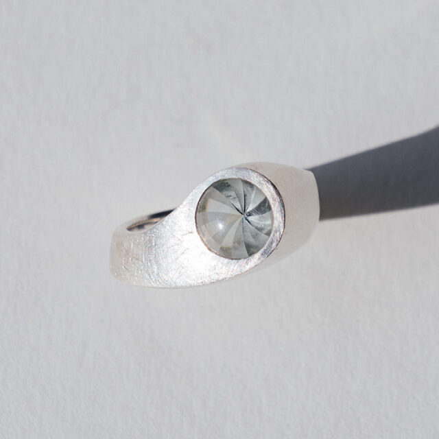 Silberner Ring mit leicht transparentem grauen Stein mit besonderem Schliff auf einem grauen Hintergrund