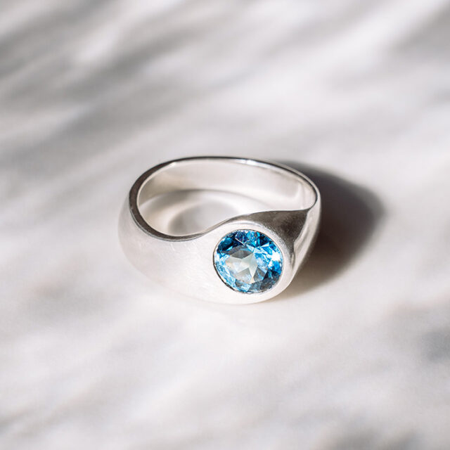 Silberner Ring mit intensiv blauem Stein auf einem grauen Hintergrund
