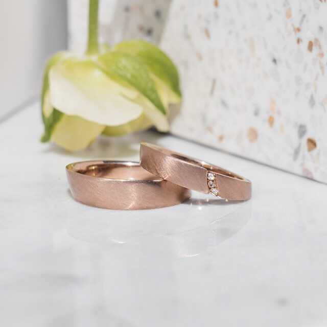 Eheringe aus 750er Roséweißgold. Der Damenring ist ein Spalt-Ring mit drei weißen Brillanten.