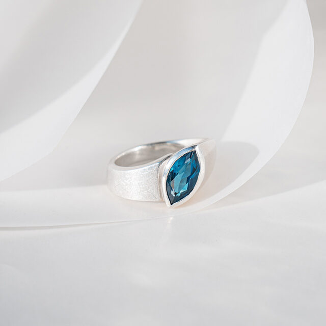 Ergonomischer Ring aus Silber mit matt strukturierter Oberfläche und großem blauen Topas im Navette Schliff