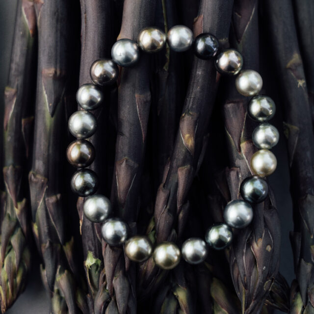 Armband mit dunklen Perlen auf Spargel gelegt