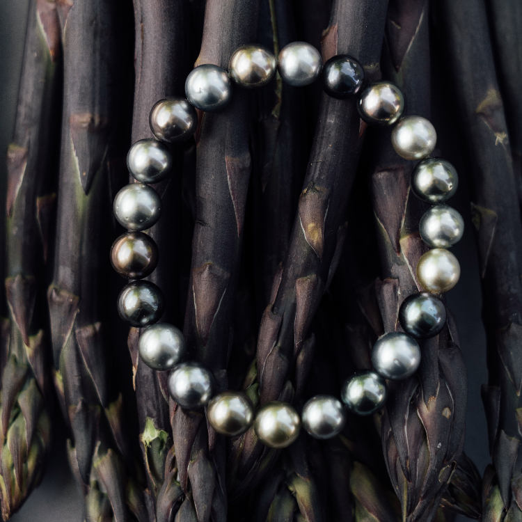 Armband mit dunklen Perlen auf Spargel gelegt