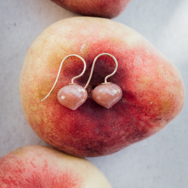 Ohrhänger mit einem braunem Stein auf einer Plattpfirsich liegend