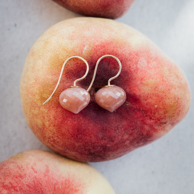 Ohrhänger mit einem braunem Stein auf einer Plattpfirsich liegend