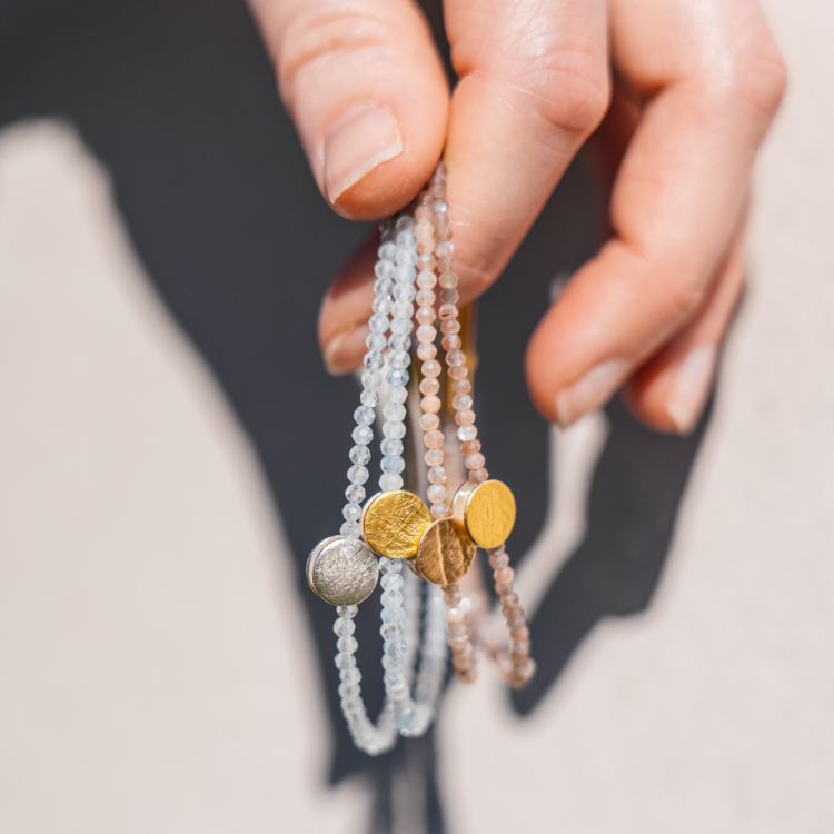 Hand hält vier Armbänder mit verschiedenen Edelsteinen und Element aus Gold und Silber