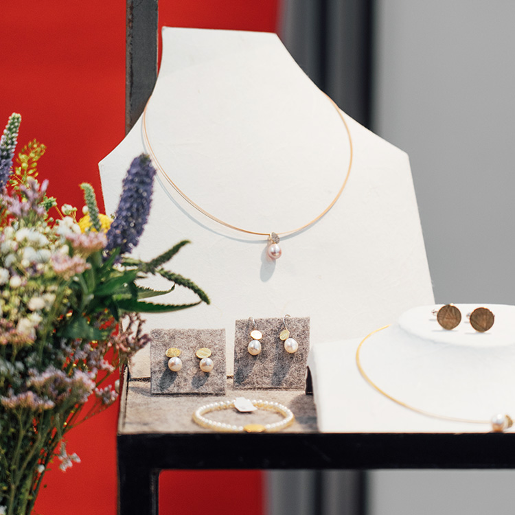 Dekorierter Schmuck auf einer Messe. Perlenohrhänger, Perlenarmband und eine Kette mit Perlenanhänger und Manschettenknöpfe sind ausgestellt.