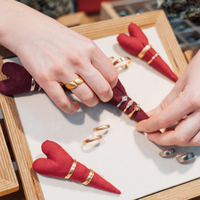 Eine Hand mit Ring greift auf einer Messe einen Ring auf einen Tablett mit weiteren Ringen.