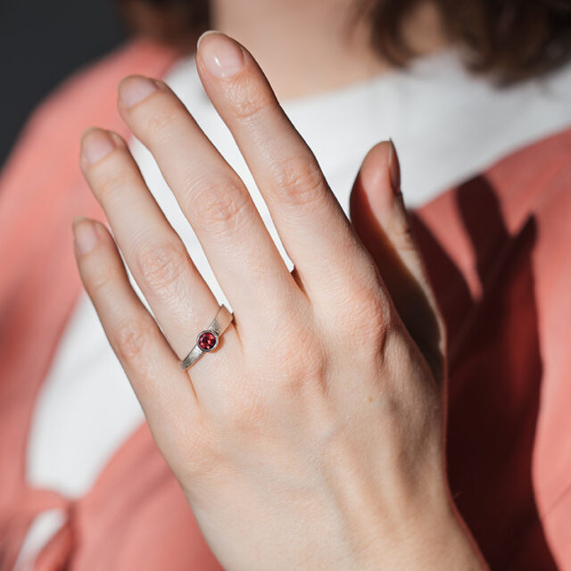 Silberner Ring mit dunkelrotem Stein an einer Hand, die in die Kamera gehalten wird.