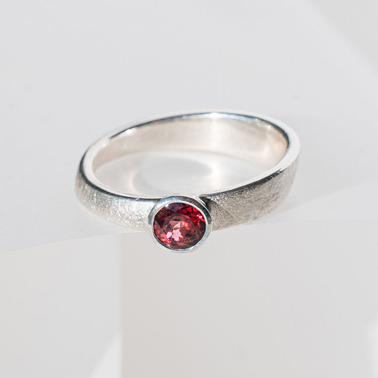 Silberner Ring mit dunkelrotem Stein auf hellem Hintergrund.