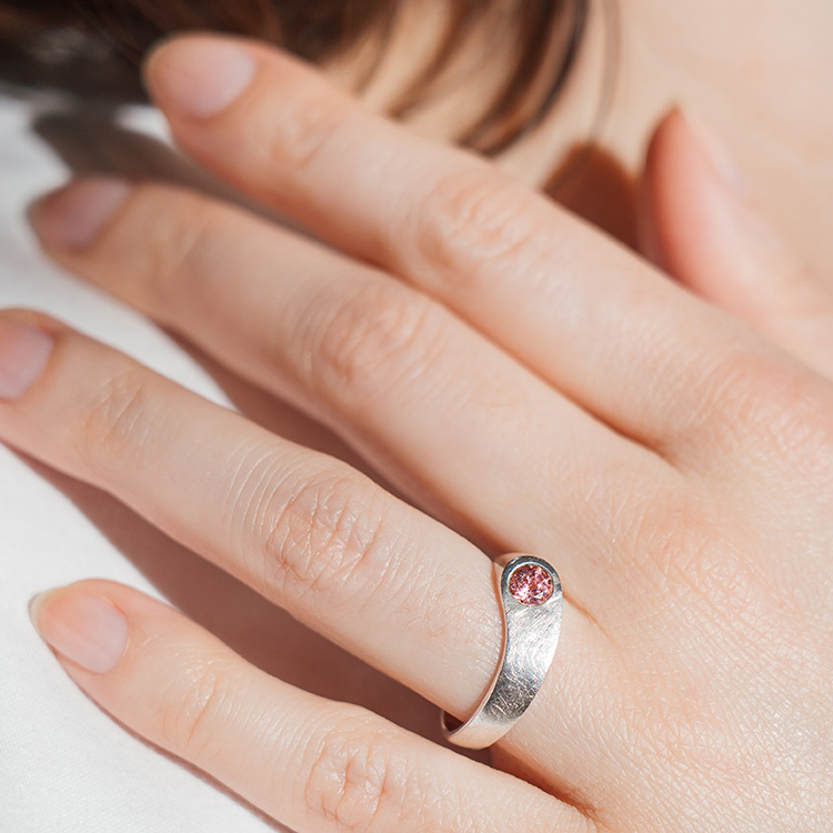Silberner Ring mit rosa Stein an einer Hand,