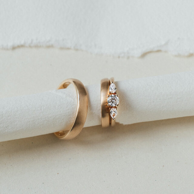 Drei goldene Ringe. Zwei Damenringe, bei denen ein klassischer Ehering mit einem Verlobungsring mit drei großen weißen Brillanten kombiniert wurde.