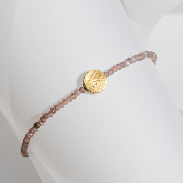 Armband mit Mondstein in warmem Braun/Orange und Element aus Gold mit strukturierter Oberfläche.