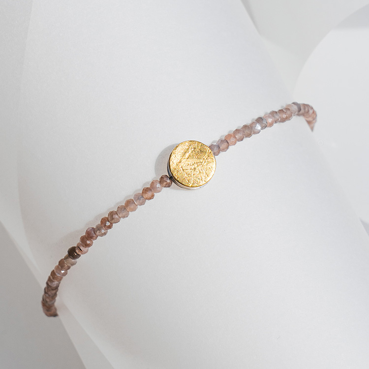 Armband mit Mondstein in warmem Braun/Orange und Element aus Gold mit strukturierter Oberfläche.