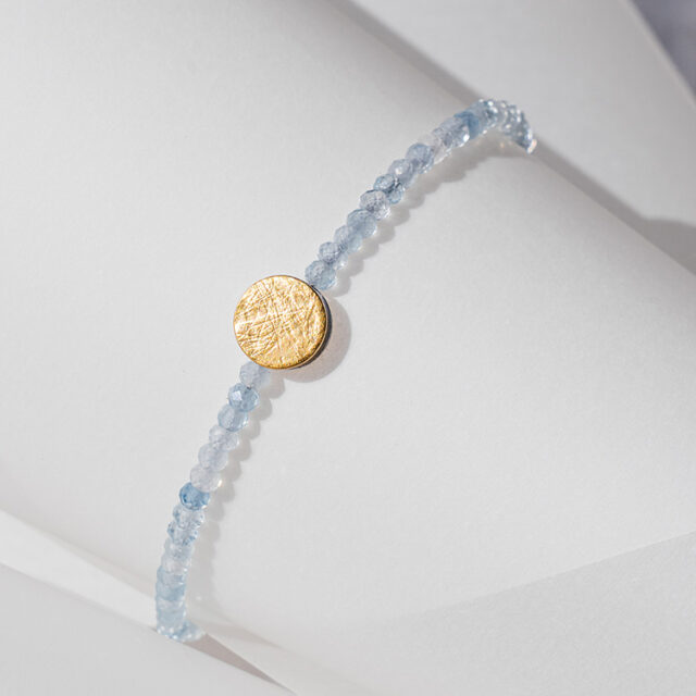 Armband mit hellblauen Aquamarin Steinen und Element aus Gold mit strukturierter Oberfläche.