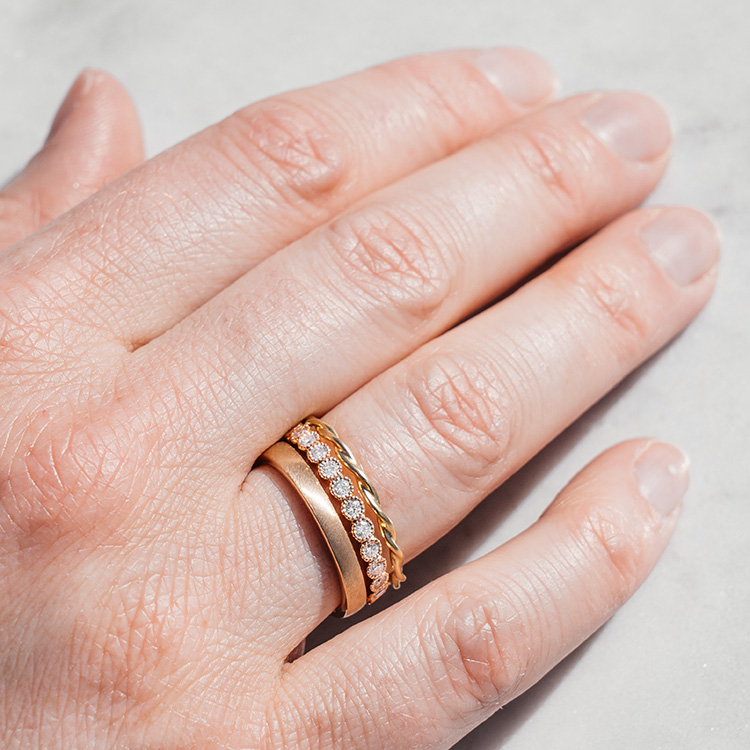 Hand mit drei Ringen am Ringfinger, ein gedrehter Kordelring, einer mit Brillanten und Millgriff Fassung und ein schlichter goldener Bandring.