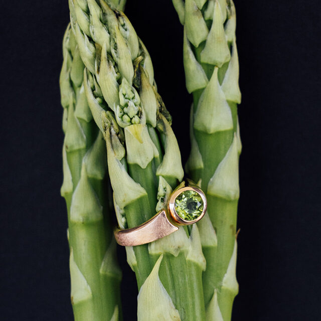 Ring in Rotgold mit Spalt und rundem Peridot gefasst auf grünem Spargel