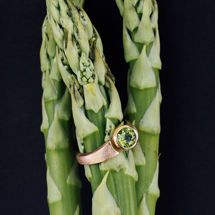 Ring in Rotgold mit Spalt und rundem Peridot gefasst auf grünem Spargel