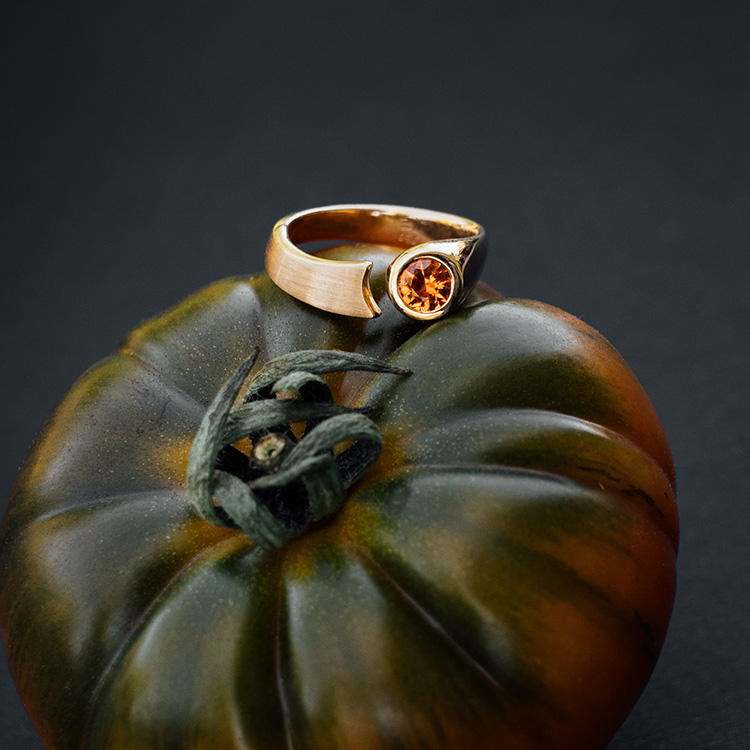 Ring in Roségold mit Spalt und rundem, orangenen Saphir auf einer grünen Tomate.