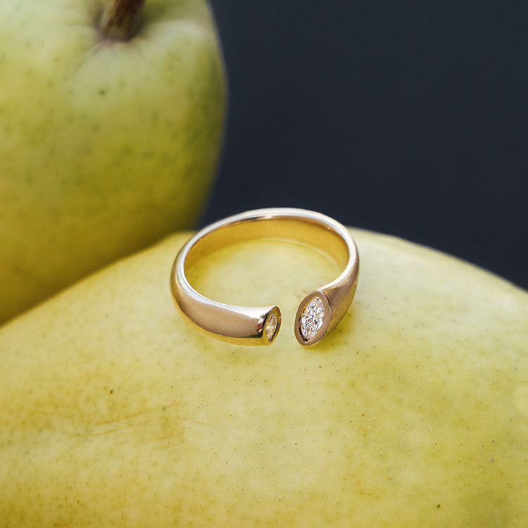 Goldener Ring mit besonderer Form mit Spalt, in die Kanten wurde jeweils ein Brillant im Navette Schliff gefasst. Der Ring liegt auf einer Birne.