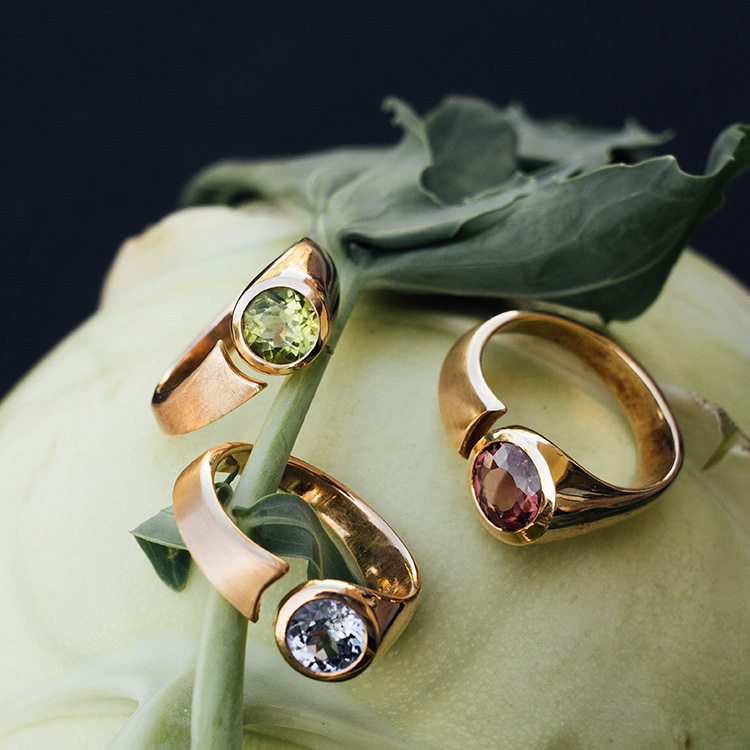 Drei Ringe in Rotgold, Roségold und Gelbgold auf einem Kohlrabi. Alle mit Spalt und Steinen in grün, blau und rosa / rot.