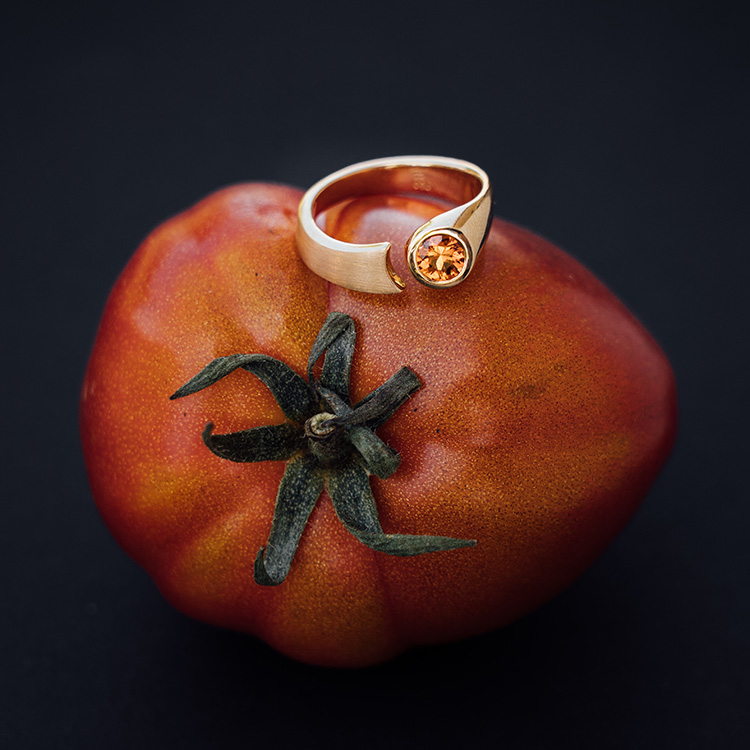 Ring in Roségold mit Spalt und rundem, orangenen Saphir auf einer roten Tomate.