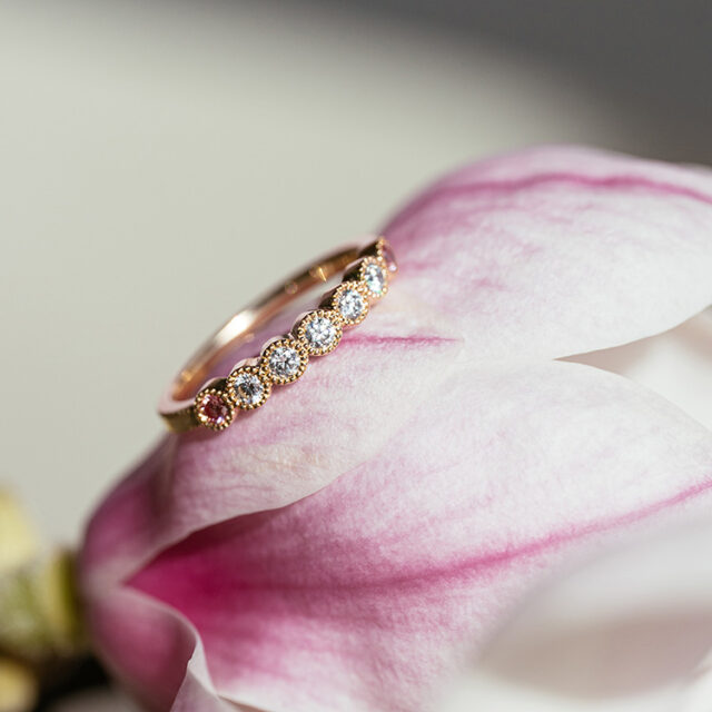 Millgriff-Ring mit filigran gefassten Brillanten in weiß und rosa liegt auf einer rosa Magnolienblüte