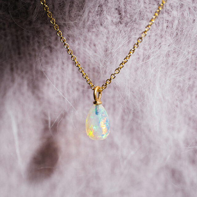 Ein facettierter Opal-Anhänger an einer Kette in Gelbgold, der in vielen bunten Farben in der Sonne schimmert.