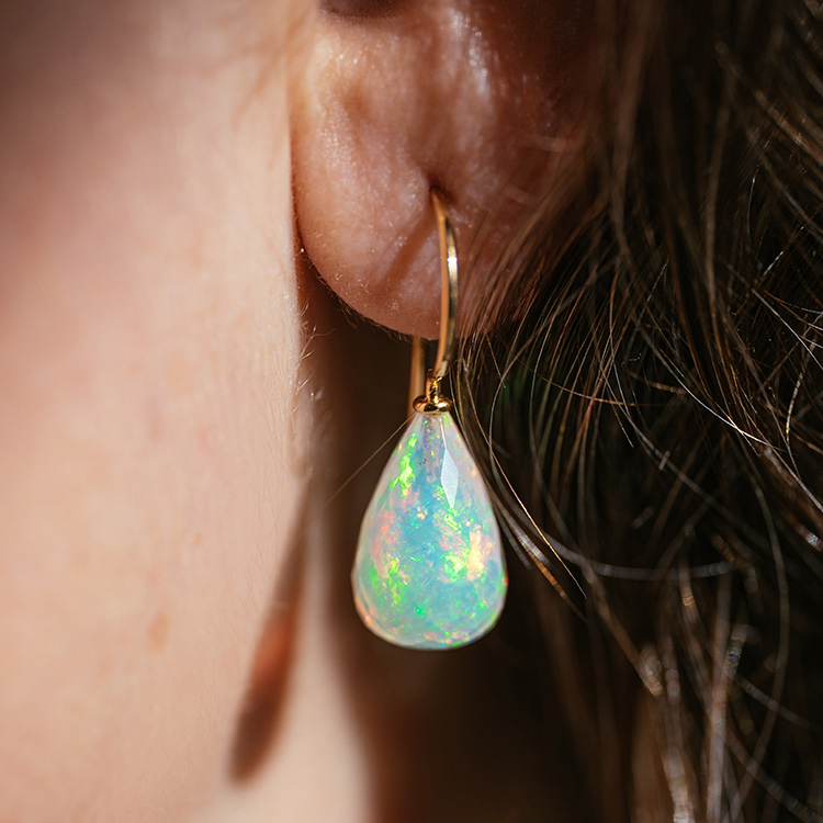 Ohrhänger mit Gelbgold und facettiertem Opal, der in verschiedenen Farben schimmert, am Ohr getragen.