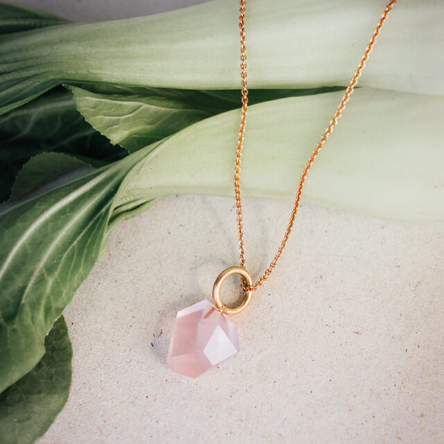 Kette aus Roségold mit Anhänger aus 585er Roségold und Rosenquarz im besonderen Klunkerschliff liegt auf einem Pak Choi