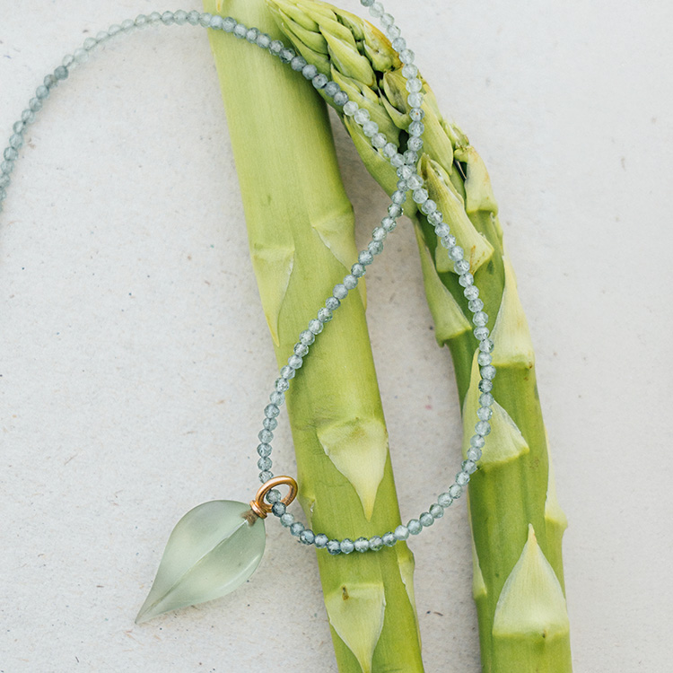 Kette aus grünen Steinen mit Anhänger aus Roségold und einem Prasiolith liegt auf grünem Spargel