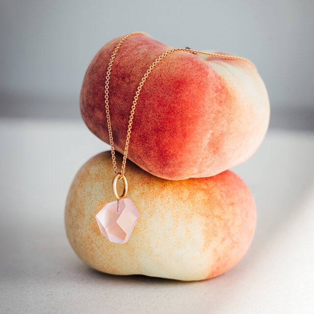 Kette aus Roségold mit Anhänger aus 585er Roségold und Rosenquarz im besonderen Klunkerschliff hängt auf zwei Pfirsichen