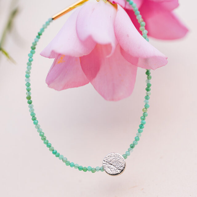 Armband mit Türkisen Steinen, Chrysopras, und rundem Punkt Element mit aufgewalzter Struktur aus Silber hängt in einer pinken Blüte.