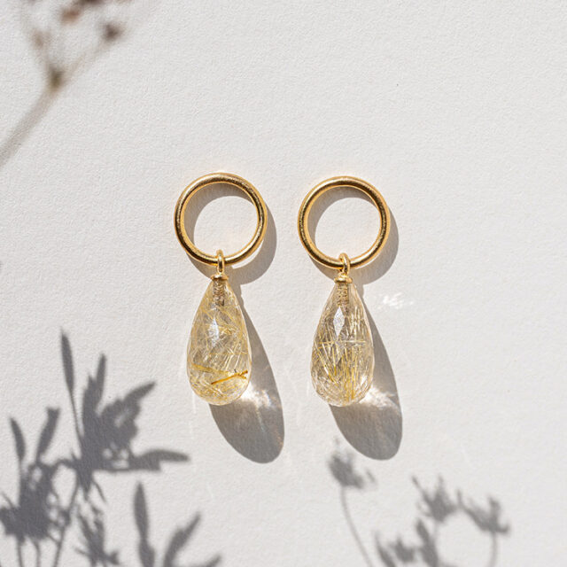 Ohtstecker mit goldenem Kreis und Rutilquarz mit goldenen Nadeln auf einem weißen Hintergrund