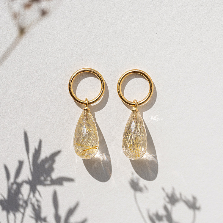 Ohtstecker mit goldenem Kreis und Rutilquarz mit goldenen Nadeln auf einem weißen Hintergrund