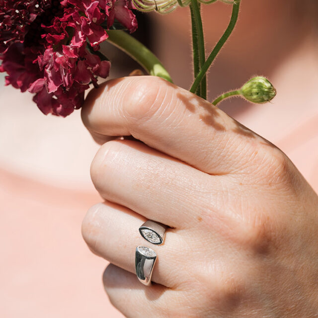 Ring mit Spalt und zwei Navette Steinen an einer Hand, die Blumen hält.